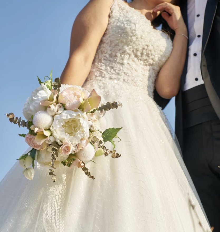 Bride holding a pastel bouquet against a clear blue sky