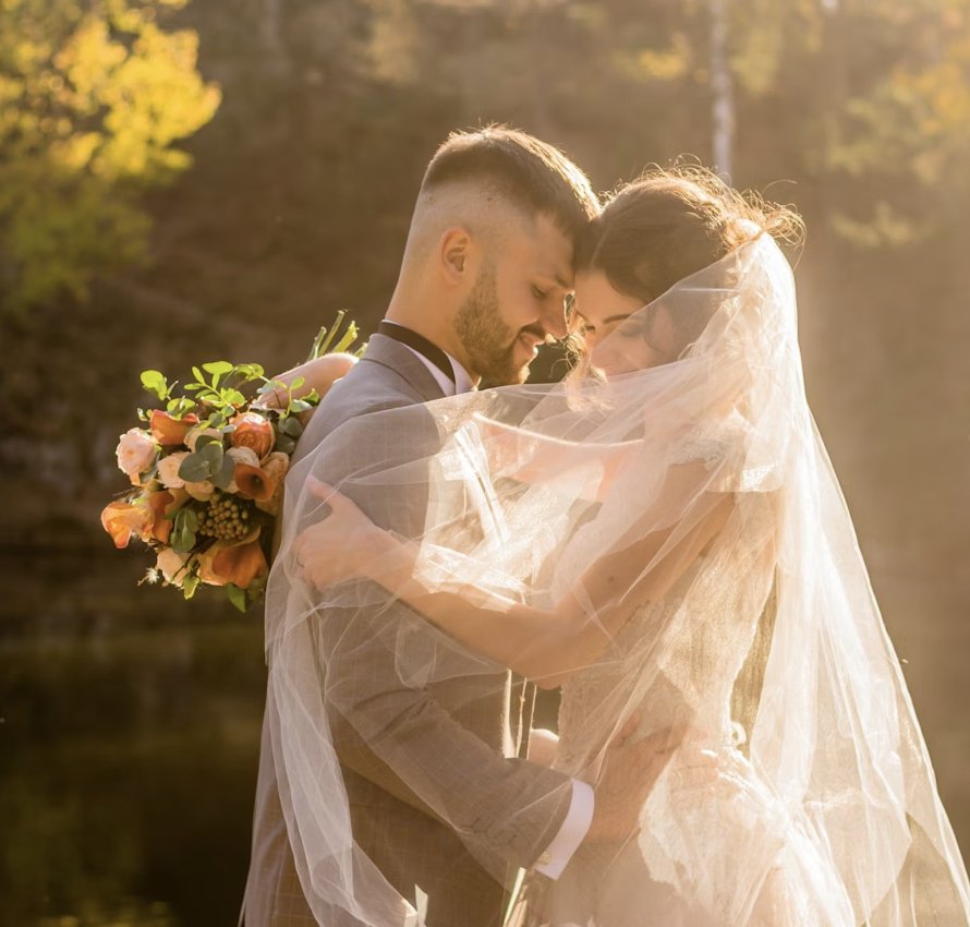 Bride and groom embracing beneath a veil in golden evening light